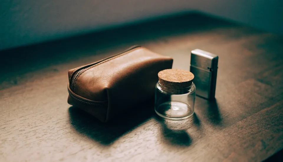 Ledertasche, Glasdose und Metallfeuerzeug auf dunklem Holz